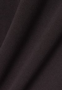 Tmavohnedá látka s textúrovaným povrchom, zobrazujúca tkaný vzor. Materiál vyzerá mäkko a hladko sa zvažuje.