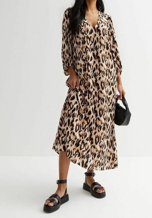 Kvinde iført en leopardprint midi-kjole med lange ærmer, sorte platformsandaler og holder en lille sort håndtaske.