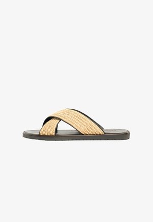 Sandalo basso con suola scura e ampie fasce beige intrecciate a incrocio, mostrato di lato su sfondo bianco.
