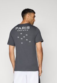 T-shirt grigio a maniche corte con testo stampato bianco "PARIS" e "PANAME" sul retro, con numeri e design classico a girocollo.