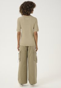 Beiger Stricktop mit kurzen Ärmeln und gewelltem Saum, kombiniert mit weit geschnittenen khakifarbenen Cargo-Hosen mit mehreren Taschen.