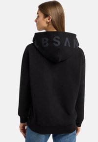 Schwarze Kapuzenjacke mit einer geräumigen Kapuze, gerippten Bündchen und einem dunkelgrauen Logo, das auf dem Rücken aufgedruckt ist. Der Stoff wirkt weich und hat eine lässige Passform.