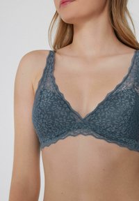 Bralette de encaje en gris pizarra con patrón floral. Presenta un escote en forma de V profundo y bordes con ondas. Fabricado con una suave tela texturizada.