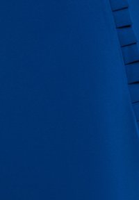 Close-up van blauwe stof met een verticale, gevouwen plooidetail langs de rechterrand.
