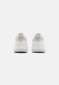 Sneaker bianche con una parte superiore in sintetico liscio, dettagli beige a contrasto sul tallone e dettagli testurizzati sulle linguette del tallone.