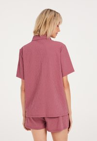 Conjunto de camisa de manga corta con cuello y pantalones cortos en tejido mauve texturizado, con un ajuste relajado y un sutil patrón de cuadrícula.