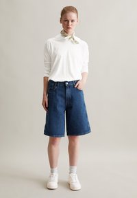 Denim shorts met een losse pasvorm, vervaagde blauwe kleur, vijf-pocket ontwerp en een knoopsluiting, gecombineerd met een wit langemouwen top en sneakers.