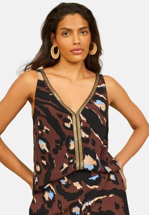 Hosszú sötét hajú nő arany karika fülbevalóval, ujjatlan barna állatmintás felsővel, amely arany szegéllyel díszített a nyakkivágásnál.