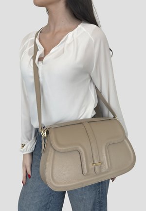 Donna che indossa una camicetta bianca e jeans blu con borsa a tracolla in pelle beige con dettagli in metallo dorato.