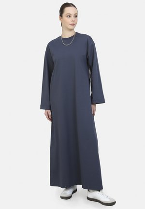 Pitkä tummansininen mekko, joka on valmistettu pehmeästä kankaasta. Mekossa on pyöreä kaula-aukko ja pitkät hihat, ja se on yhdistetty valkoisiin tennareihin kontrastiksi.