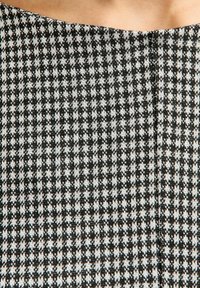 Schwarz-weiß kariertes Strickgewebe mit einer glatten Textur, das über einen weiten Ausschnitt und eine subtile Naht verfügt, die vertikal verläuft.