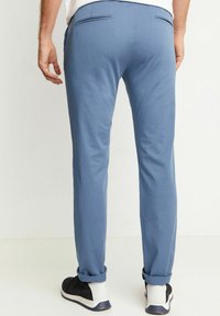 Světle modré kalhoty se slim fit, vyrobené z hladkého materiálu, se zadními kapsami a ohrnutými nohavicemi. Nošeny s černo-bílými teniskami.