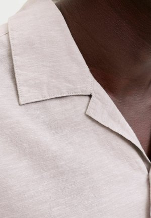 Primer plano del cuello de una persona que lleva una camisa de color beige claro con cuello y costuras visibles sobre piel oscura.