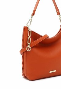 Sac à bandoulière en cuir orange avec détail chaîne en or et petit charm rond, avec un bord cousu et une plaque de marque dorée.