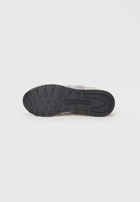 Reebok sportinių batelių padas juodos gumos su tekstūruotu sukibimu, kuriame yra prekės ženklas ir apvalių bei ovalių įdubimų raštas.