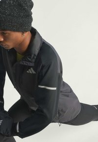 Black athletic jacket with gray accents, lightweight material, high collar, and zip closure. Black knit beanie with textured pattern.