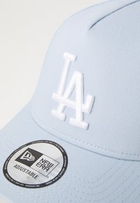 Gorra de béisbol azul claro con un logo bordado en blanco que dice "LA". Presenta una textura de tela suave y una correa ajustable en la parte posterior.
