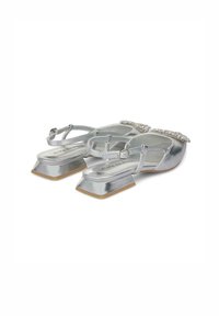 Silberne metallische flache Schuhe mit einem quadratischen Absatz, ausgestattet mit einem mit Strass besetzten Riemen und einer glatten Oberfläche. Die Sohle ist beige.
