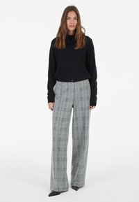 Black knit cowl-neck sweater paired with light gray and black check-pattern wide-leg trousers, featuring front pockets and a tailored fit.
