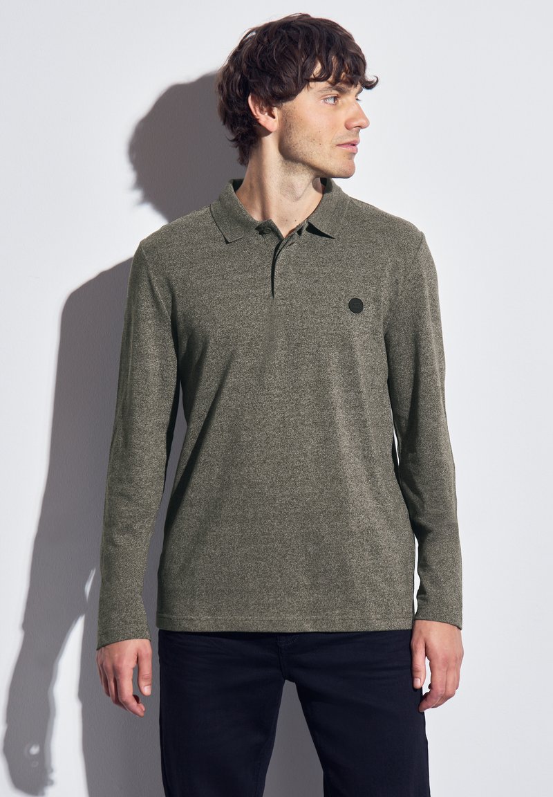 Polo à manches longues en vert olive, fabriqué en tissu texturé. Il présente un col classique et un petit logo noir sur la poitrine.
