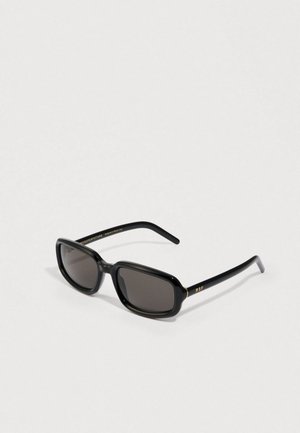 Black sunglasses with an oval frame, dark lenses, and gold accents on the temple. Made of plastic with a glossy finish.