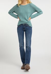 Svetle tyrkysový pletený svetr s širokým výstřihem, v kombinaci s modrými rovnými džíny a hnědými kotníkovými botami. Jednoduchý, neformální outfit.