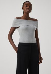Grå av-hullet ribbet topp med tettsittende design, kombinert med svarte vide bukser. Rask tekstur og minimalistiske stil detaljer.