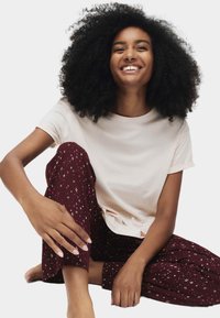 Camiseta de manga corta rosa claro combinada con pantalones burdeos que presentan patrones geométricos en blanco y rosa, mostrando un ajuste relajado y una tela suave.