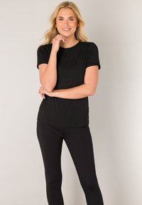 Schwarzes T-Shirt mit kurzen Ärmeln aus weichem Stoff, mit lässiger Passform und Rundhalsausschnitt, kombiniert mit schwarzen Leggings.