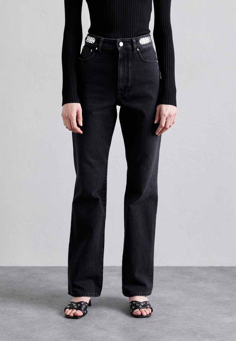 High-waisted black jeans with a straight leg design, featuring front pockets, metal hardware, and a contrasting logo on the waistband.