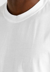 Witte katoenen T-shirt met een ronde hals, een zachte textuur en minimale stikdetails langs de kraag. Casual ontwerp, geen patronen of accenten.