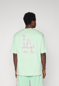 Mint green cotton t-shirt features a large LA logo with floral patterns on the back, alongside "Los Angeles Dodgers" in script below.