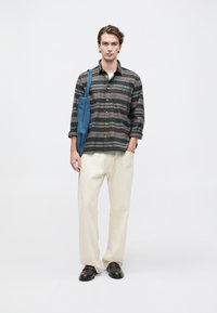 Koszula z guzikami w czarne i szare paski, kremowe spodnie o szerokich nogawkach, ciemne buty oraz niebieska torba z płótna.