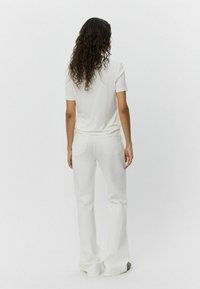 Tricou alb cu mâneci scurte, asortat cu pantaloni albi evazați cu talie înaltă. Textură de țesătură netedă, design minimalist, detalii subtile pe cusătura din spate.