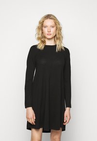 Abito lungo nero a maniche lunghe con vestibilità morbida, scollatura rotonda e texture liscia. Si ferma sopra il ginocchio con dettagli di cucitura sottili.