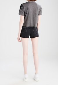 Camiseta gris recortada de mangas cortas, combinada con pantalones cortos de mezclilla negros. Ambos son simples, con detalles mínimos. Zapatillas blancas completan el look.