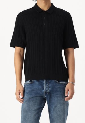 Sort kortærmet polo-shirt med ribbet tekstur, tre-knaps placket og en blød krave, parret med blå denim jeans.