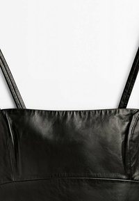 Gros plan d'un top en cuir noir avec fines bretelles et détails cousus sur fond blanc.
