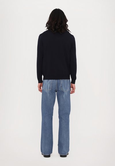 Tengerész kék pulóver és világoskék bő szabású farmernadrág. A pulóvernek kerek nyaka, hosszú ujja van, és sima textúrájú; a farmernadrágnak hátsó zsebei és kopott területei vannak.