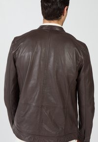 Bruine leren jas met een glad oppervlak, een aansluitend model en subtiele stiksel details op de schouders en rug. Geen zichtbare metalen onderdelen.