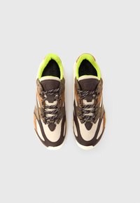 Zapatillas deportivas marrones y beige con parte superior de malla, detalles en neón verde contrastante y cordones con patrón en blanco y negro.