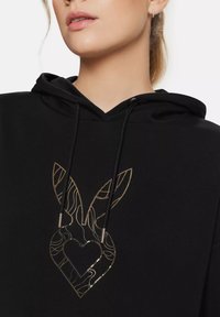 Black hoodie featuring a metallic gold graphic of bunny ears and a heart design. Includes drawstrings with silver aglets. Soft texture.