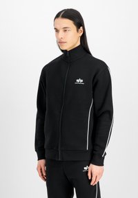 Svart zip-up hettegenser med høy krage, hvite sidestriper og logo p�å brystet. Laget av myk stoff med en avslappet passform.