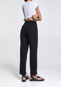 Svarta högmidjade byxor med elastiskt midjeband, uppvikta fållar och två bakfickor. I kombination med platta svarta sandaler och en vit åtsittande topp.