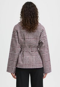Giacca a quadretti con cintura, caratterizzata da un motivo rosso e bianco. Vestibilità ampia, maniche larghe, realizzata in tessuto testurizzato.
