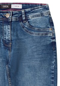 Ciemnoniebieskie dżinsy z lekko wyblakłym wyglądem, z metalowym guzikiem, żółtymi szwami i metką z napisem "CECIL DENIM".
