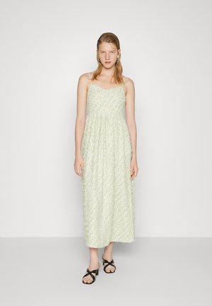 Vestido midi de cor verde claro, com alças finas, apresentando aplicações florais texturizadas. Usado com sandálias pretas. Brincos de argola.