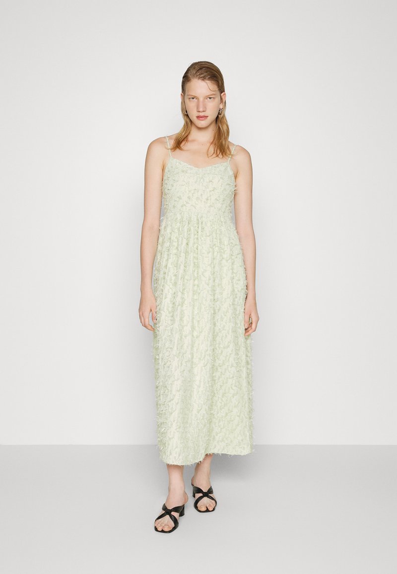 Vestido midi de cor verde claro, com alças finas, apresentando aplicações florais texturizadas. Usado com sandálias pretas. Brincos de argola.