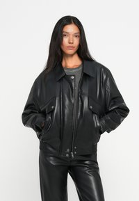 Veste en cuir noir avec un design à col, fermeture zippée sur le devant et deux poches poitrine, associée à un pantalon en cuir assorti.