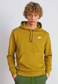 Sweatshirt amarelo mostarda com um bolso frontal e capuz ajustável. Apresenta um pequeno logotipo branco da Nike no peito. Textura de tecido suave.